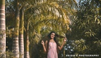 a beautiful woman in a pink dress standing in a park with palm trees